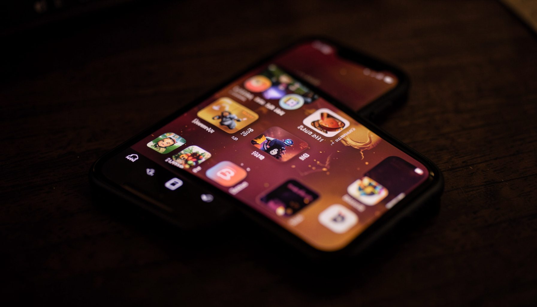 A softly lit mobile phone screen glowing with warm maroon and gold tones on a dark wooden desk, evoking a quiet evening spent browsing game apps