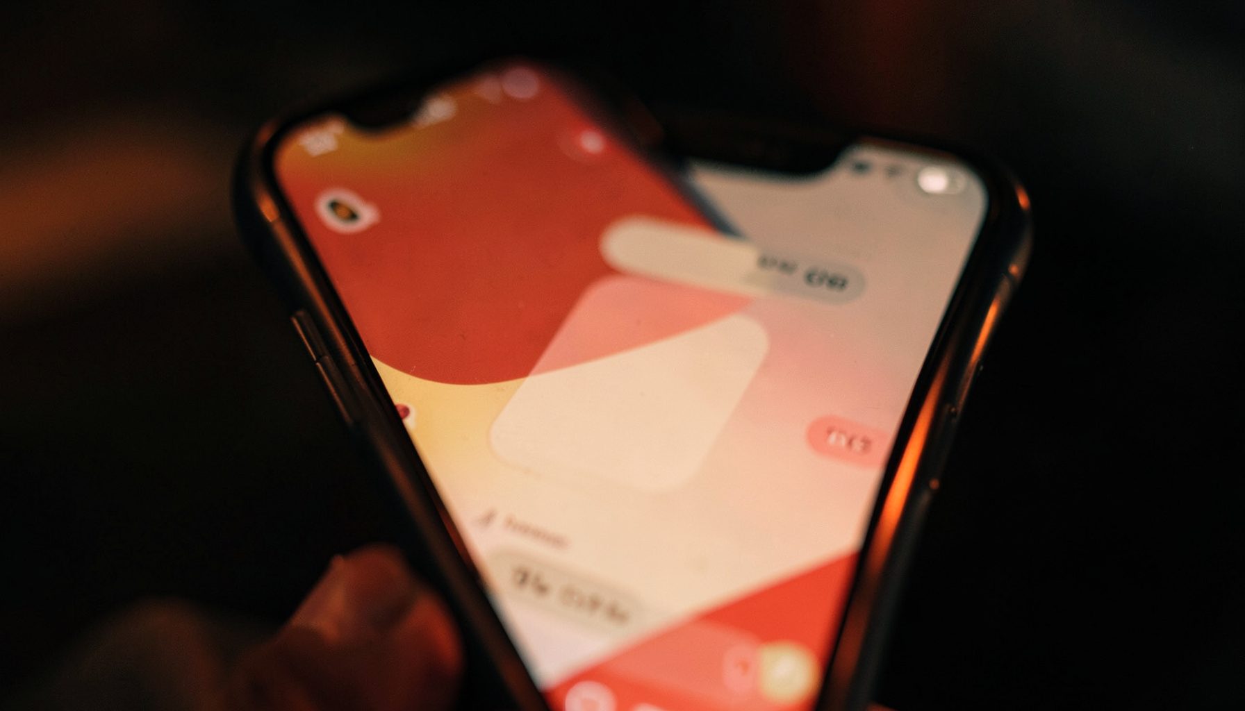 A warm-toned close-up of a smartphone screen displaying a messaging interface, with soft amber and deep red accents against a dark blurred background